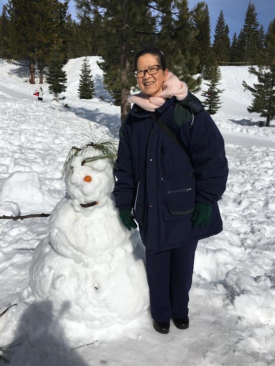 A person stands next to a snowman in a snowy mountain area, enjoying winter weather.