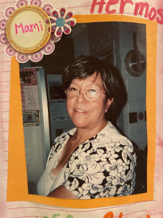 A woman with glasses and a warm smile enjoys a family gathering in a bright kitchen setting.