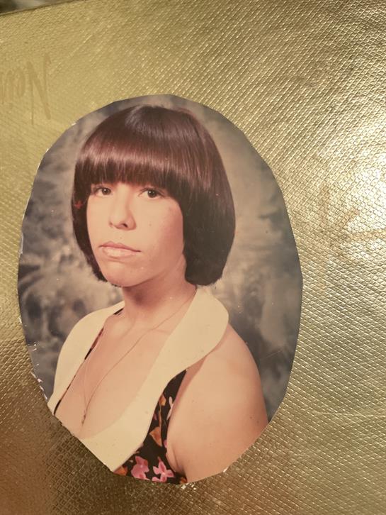 A woman poses with a bob haircut and a patterned outfit, showcasing a retro style from the 1970s.