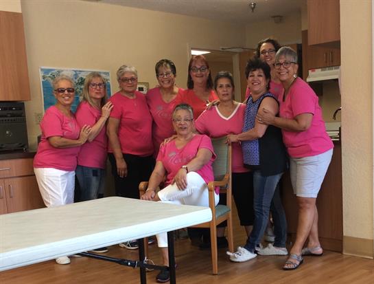 A joyful gathering of women wearing pink shirts enjoys a fun moment at a community center.
