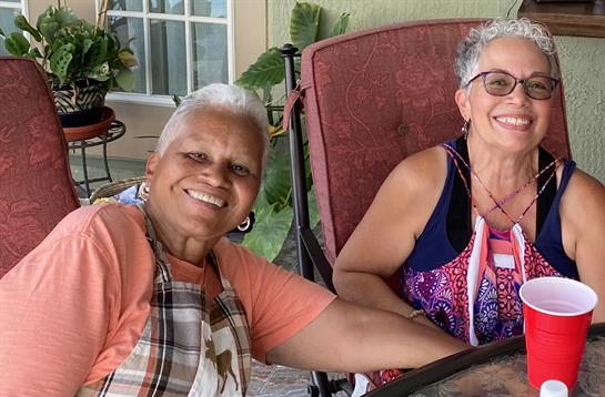 Two cheerful women sit together on a patio, sharing a joyful moment in the sun.