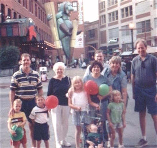 Group of eleven individuals poses together outside with balloons on a sunny day in the city.
