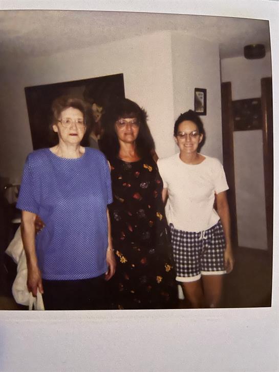 Three women stand close together, smiling in a welcoming home environment showcasing family bonds.