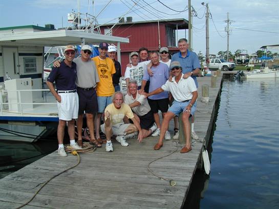 A group of men gather on a dock, smiling and posing together during a sunny summer day.
