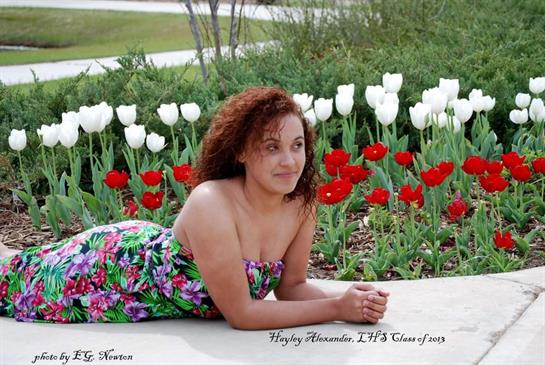 A woman lies on the ground, surrounded by blooming red and white tulips in a garden.