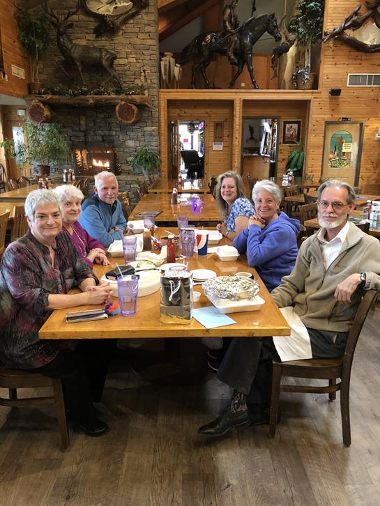 Six friends gather around a wooden table sharing food and laughter in a rustic dining space.