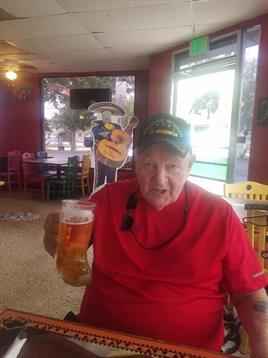 An older man enjoys a cold beer while seated in a lively diner with bright decorations.