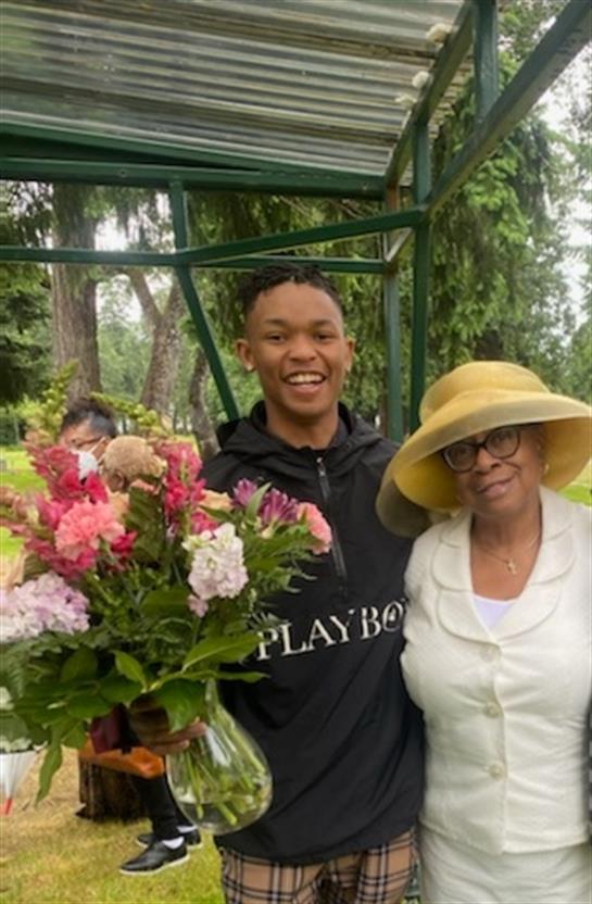 A young man smiles while giving a beautiful bouquet to a woman in a garden setting.