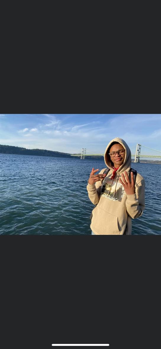 A hoodie-clad youth gestures by the river, enjoying the pleasant weather.