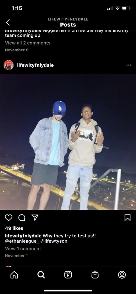 Two friends posing together on a rooftop during nighttime with city lights in the background.