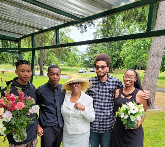 Group of five family members joyfully posing outdoors in a park holding flowers.
