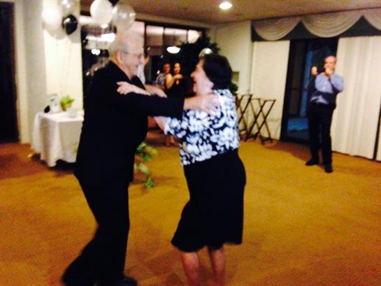 A couple dances joyfully in a decorated ballroom while guests celebrate an evening event.