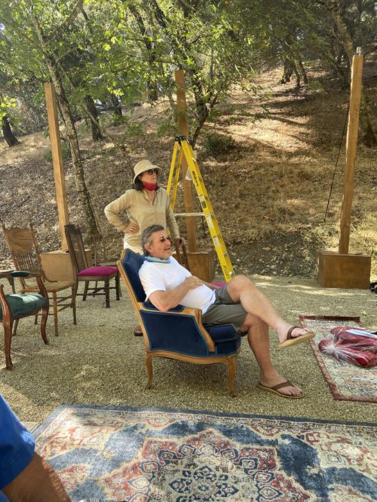 Two individuals enjoy a leisurely outdoor gathering surrounded by trees, with chairs and decor.