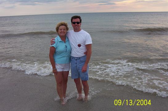 A couple stands together in shallow water, enjoying the sunset at a serene beach.