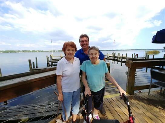 Three family members stand together on a dock, smiling and enjoying a cheerful day by the water.