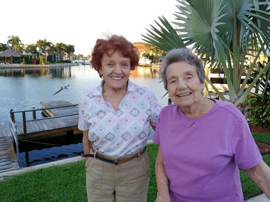 Older women are enjoying each other's company near a serene waterfront at sunset.