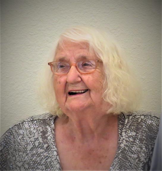 An elderly woman smiles warmly, radiating joy in a cozy indoor environment.