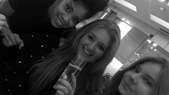 Three friends smile and toast with drinks while having a good time in a stylish lounge.