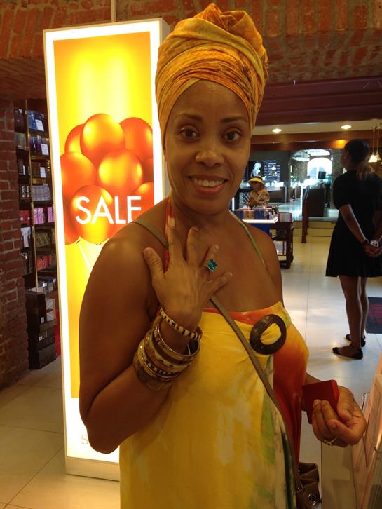 A woman proudly displays her colorful jewelry while shopping in a busy mall setting.