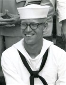 A young sailor in uniform enjoys a light moment while seated at a summer naval event.