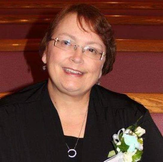 A cheerful woman wears a black outfit and a white flower corsage while smiling at a gathering.