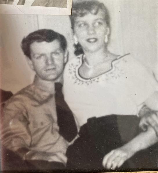 A couple shares a warm moment at a gathering, embracing vintage fashion and affection.