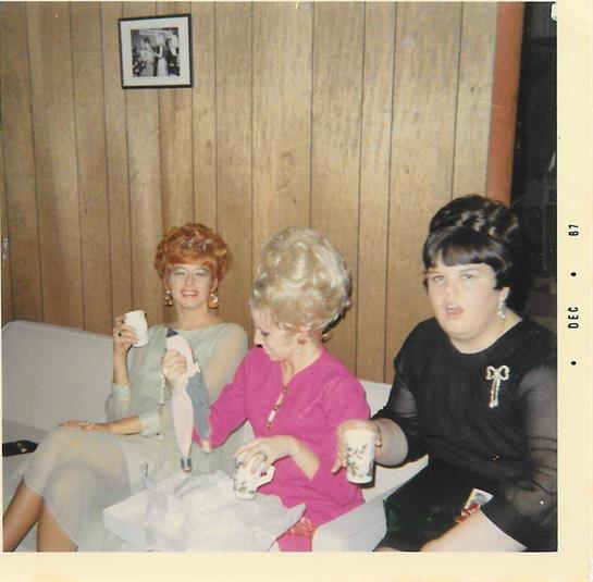 Stylishly dressed women are gathered, holding drinks at a lively event.