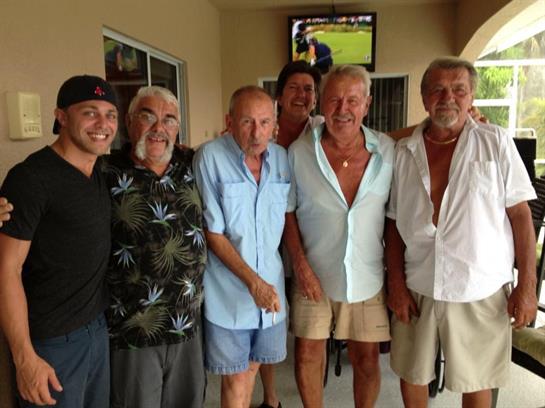 A group of six men stands together, smiling and enjoying camaraderie in a relaxed atmosphere.
