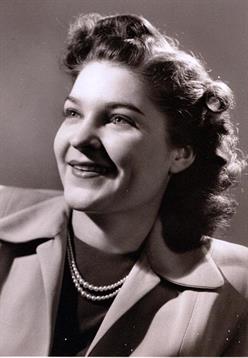 Smiling woman poses confidently with a vintage hairstyle and elegant pearls, exuding style.