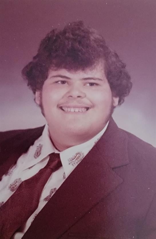 Confident young man in a formal outfit and patterned tie smiles for a school portrait.