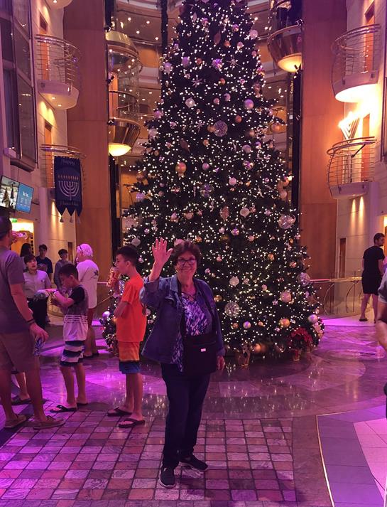 People gather by a decorated Christmas tree in a busy shopping area, embracing the holiday spirit.