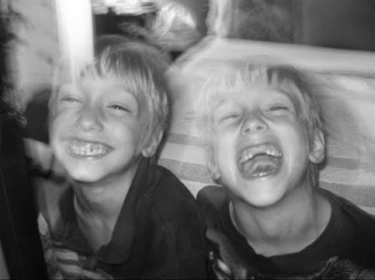 Two young children laugh together indoors, creating a joyful atmosphere.