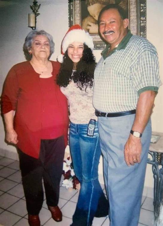 Three family members pose together, showcasing festive attire and smiles in a warm home.