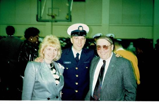 A proud graduate in uniform stands with his parents, celebrating a milestone achievement together.