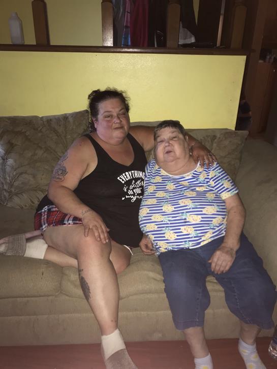 Two women are sitting comfortably on a couch, smiling and relaxing together in a cozy living area.