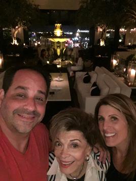Three friends smile while dining at a stylish restaurant in a vibrant city atmosphere.