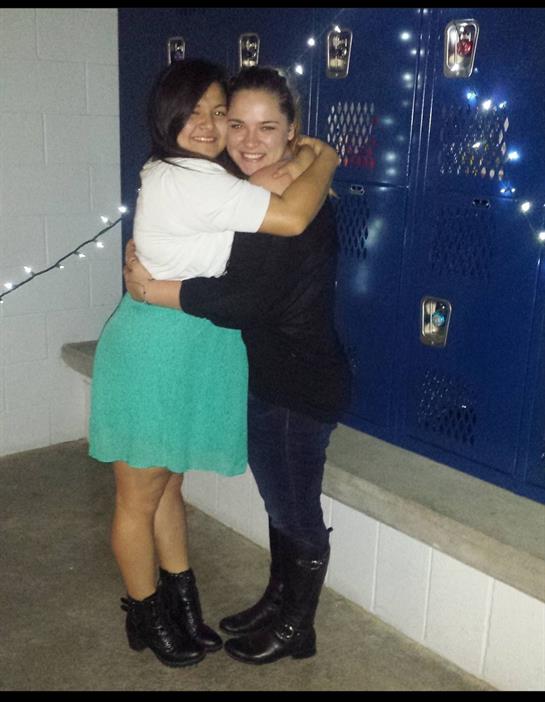 Two friends share a happy moment as they hug in a school corridor filled with decorations.