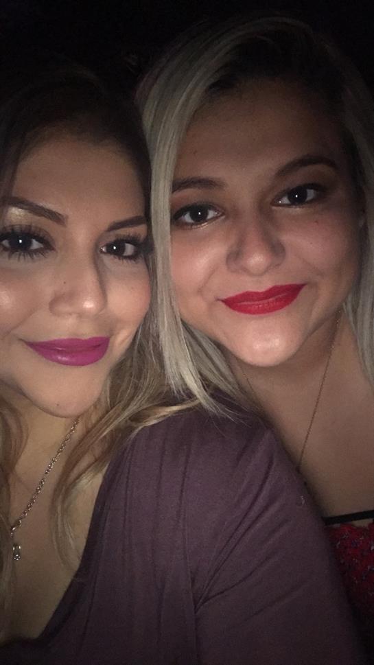 Two friends pose closely together, smiling brightly with vibrant lipstick in a casual atmosphere.