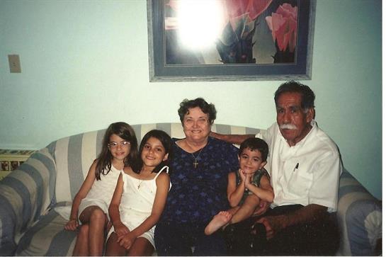 Grandparents sit with four children on a sofa, sharing smiles and laughter in a cozy living room.