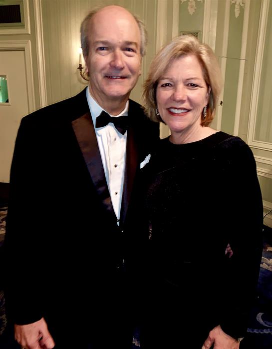 A couple in formal wear smiles together in a decorated venue during a festive event.