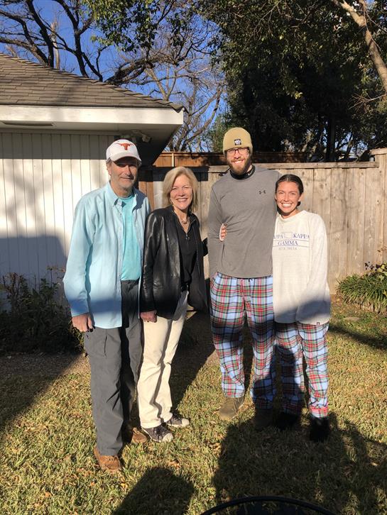 Four people stand together in a backyard wearing relaxed clothing, enjoying a sunny winter day.