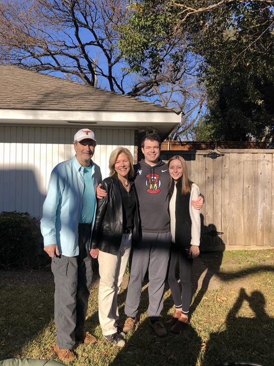 Four family members smile together in a backyard under clear winter skies, enjoying their time.