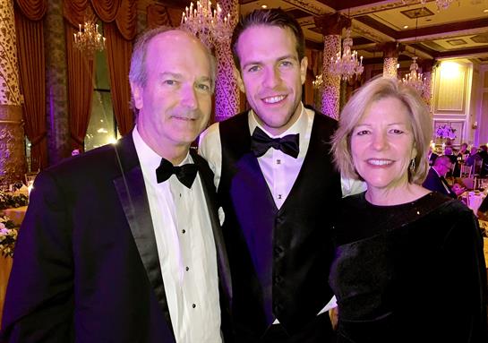 Three elegantly dressed individuals pose together in a well-decorated venue during an evening event.
