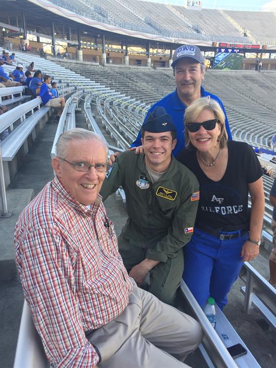 A group of four people gather in a stadium, celebrating military service and sharing smiles.