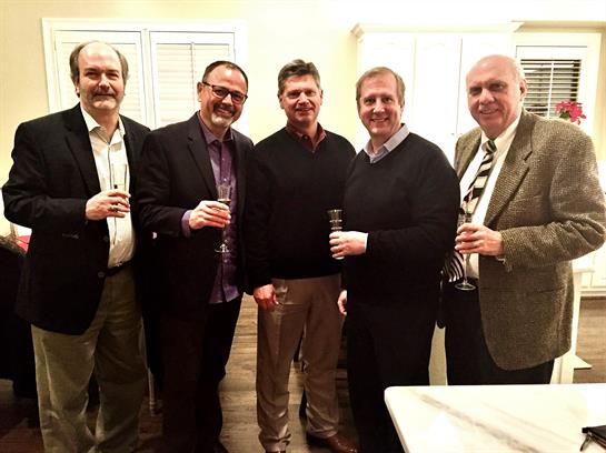 Five men are enjoying drinks and engaging in conversation at a casual indoor event setting.