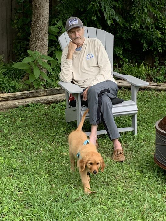 A man enjoys his afternoon in the backyard while a playful puppy explores around him.