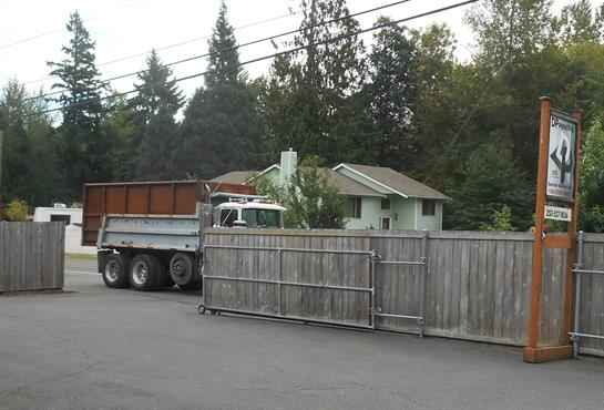 A large truck is parked next to a house, preparing to unload building materials amidst greenery.