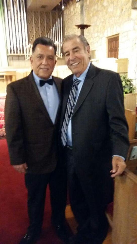 Two friends pose happily together in formal attire during a celebratory event in a hall.