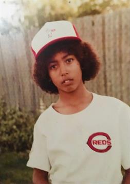 A young boy poses in a backyard, wearing a baseball cap and a t-shirt featuring a logo.