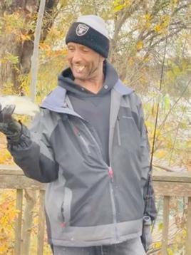 A man proudly shows off a freshly caught fish against a backdrop of colorful autumn leaves.